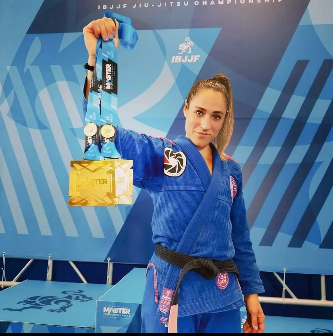Amandine Layec en kimono bleu et ceinture noire, levant ses médailles IBJJF
