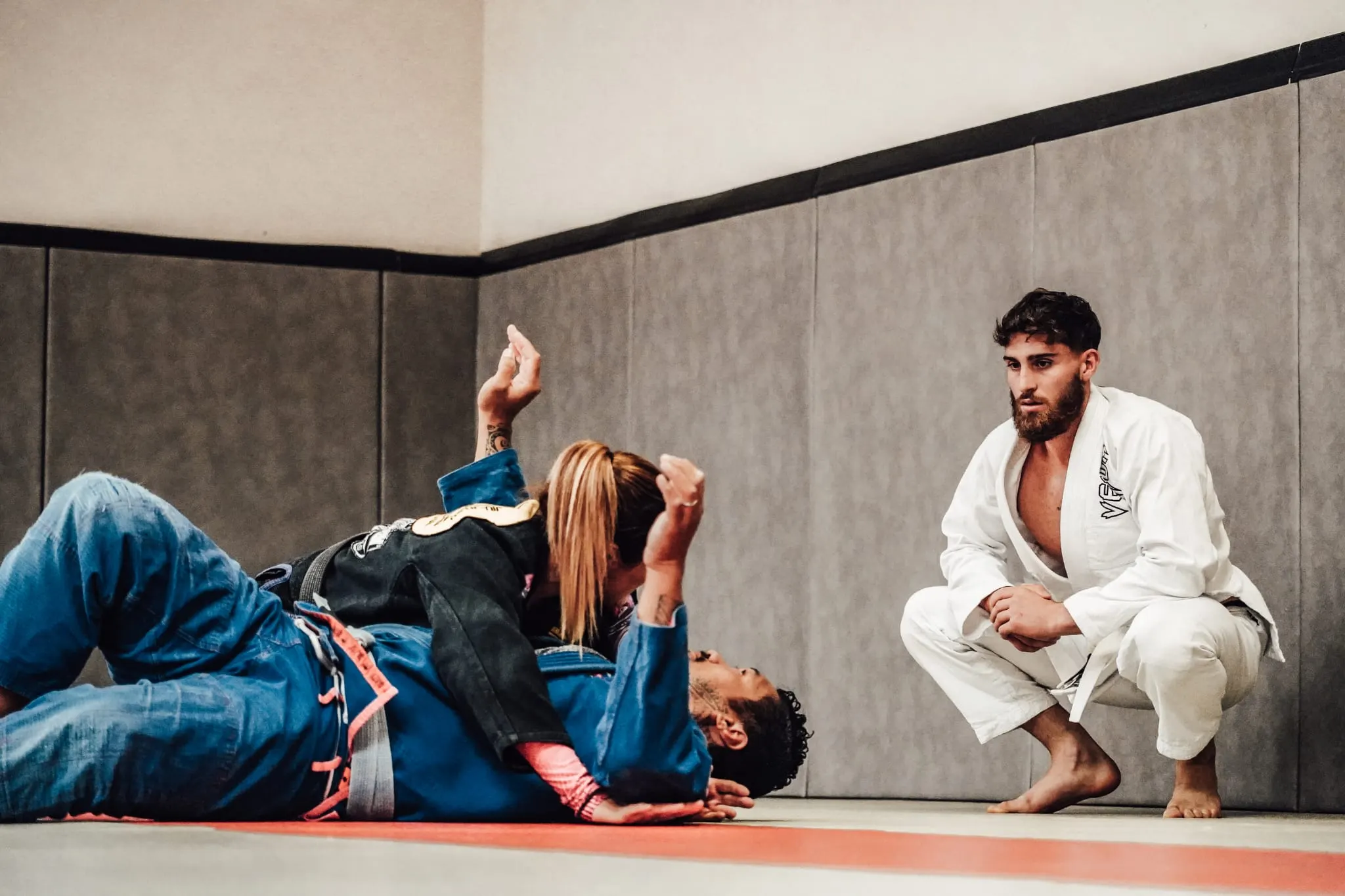 Cours au sol : une élève en kimono bleu travaille avec son partenaire, observée par un pratiquant en kimono blanc